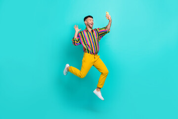 Fototapeta na wymiar Full length photo of positive cheerful man dressed striped shirt yellow pants video call smartphone isolated on turquoise color background