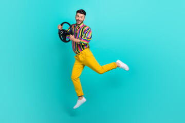 Fototapeta na wymiar Full length photo of playful handsome man dressed striped shirt yellow pants hold steering wheel isolated on turquoise color background