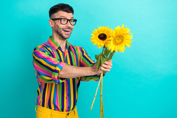 Portrait of funky cheerful man hands hold sunflowers give empty space isolated on teal color background