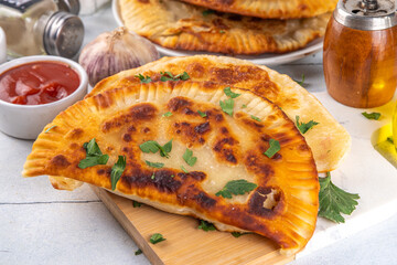 Chebureks, empanadas. Fried pies pasties, with meat and spices, on a white tiled background with herbs and tomato sauce 