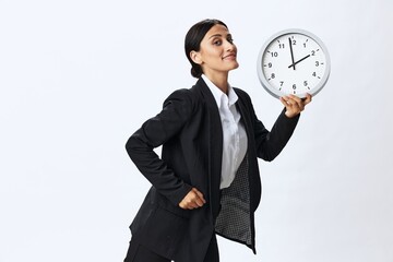 Business woman holding a wall clock in a black business suit and glasses showing signals gestures...