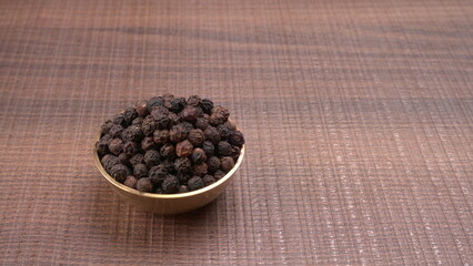 Fototapeta na wymiar Black pepper in clay bowl on wood background with copy space. Healthy eating, ayurveda, naturopathy concept.