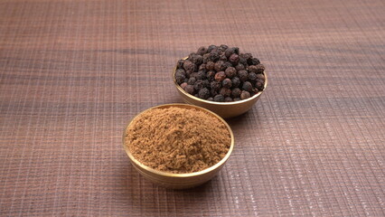 Black pepper in clay bowl on wood background with copy space. Healthy eating, ayurveda, naturopathy concept.