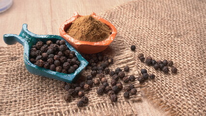 Black pepper in clay bowl on wood background with copy space. Healthy eating, ayurveda, naturopathy concept.