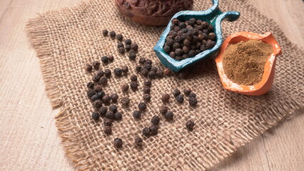 Black pepper in clay bowl on wood background with copy space. Healthy eating, ayurveda, naturopathy concept.