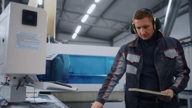 factory worker is programming a CNC milling machine, making chipboard or wooden detail for furniture
