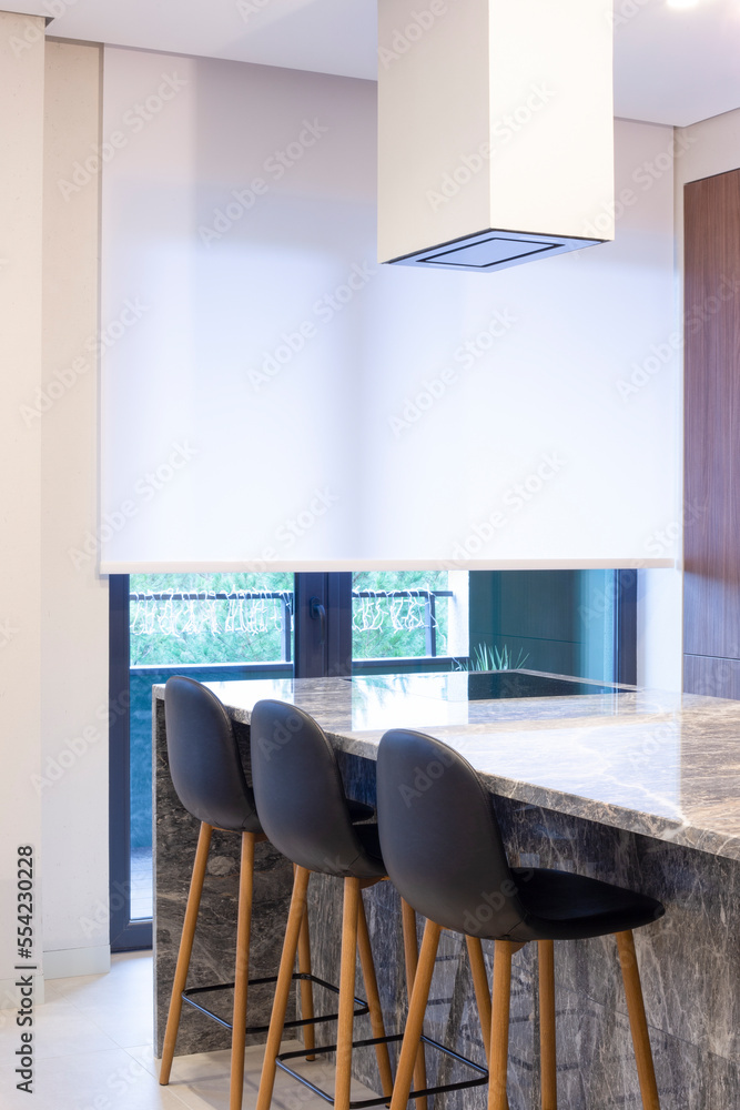 Aufkleber Roller blind large size on the window in the interior. Motorized roller shade white color in the kitchen. Bar counter with built-in hob and hood above it are near the window. Smart home concept. 