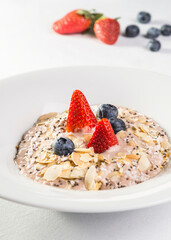 Oatmeal with almonds, blueberries and strawberries in a white plate on a white background