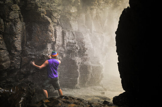 brave man entering powerful wide waterfall with white foaming water from a cave below