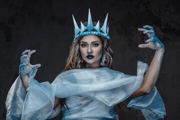 Studio portrait of snowy ice queen with cloak conjuring against dark background. - obrazy, fototapety, plakaty