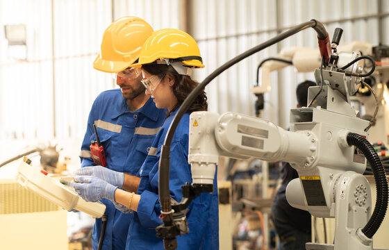 Male industrial engineer using remote control board to check robotic welder operation in modern automation factory. Woman technician monitoring robot controller system for automated steel welding.