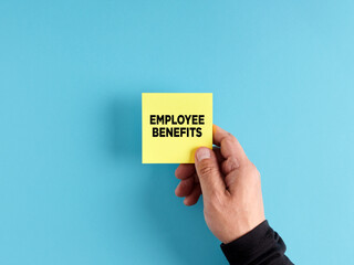 Male hand holds a yellow sticky note paper with the word employee benefits.