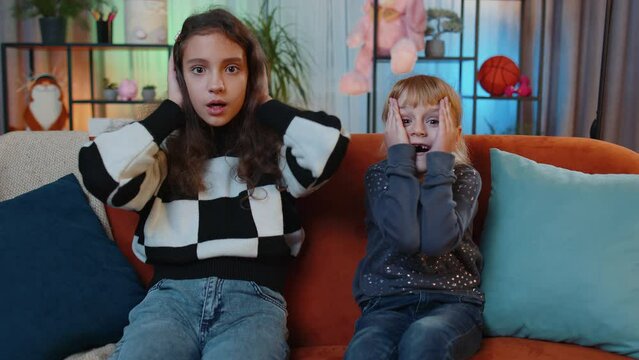 Wow. Excited amazed child and little sister kid girls surprised looking at camera with big eyes, shocked by sudden victory, good lucky win news, celebrating. Siblings children or best friends at home