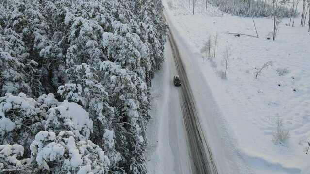 Snow covered rural road near forest with car passing by. Drone winter footage