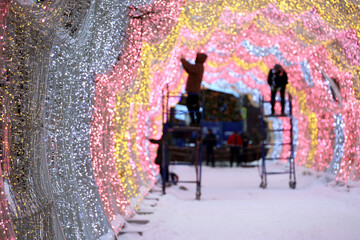 New Year ornaments on city street, workers decorating illuminated arch in winter city. Preparing for Christmas holidays