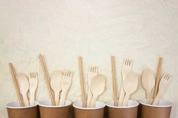 Plastic free concept. Disposable bamboo cutlery in disposable paper cups on canvas background. Flat...
