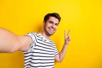 Portrait of nice satisfied young man take selfie demonstrate v-sign isolated on yellow color...