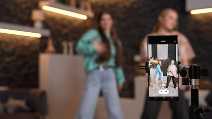 Female teens dancing together at home, recording a dance video for social media on smartphone camera. Young bloggers blurry on background making content for their channel. High quality footage. - Powered by Adobe