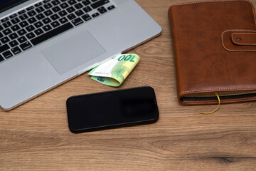 Businessman's desk. On a wooden table lies a laptop, a smartphone, money and a notebook