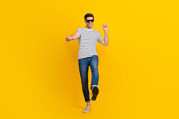 Fototapeta na wymiar Full length photo of positive cool guy dressed striped t-shirt dark eyewear dancing having fun isolated yellow color background