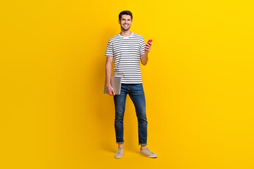 Fototapeta na wymiar Full length photo of cool pretty guy dressed striped t-shirt working apple samsung modern device isolated yellow color background