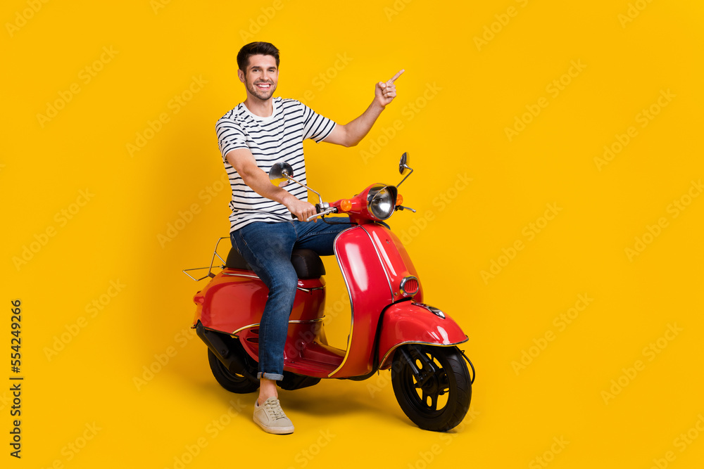 Poster full length photo of positive pretty guy dressed striped t-shirt riding moped pointing empty space i