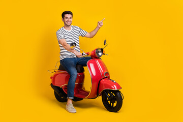 Full length photo of positive pretty guy dressed striped t-shirt riding moped pointing empty space isolated yellow color background © deagreez