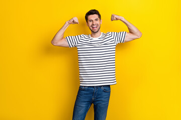Portrait of satisfied nice young man hands flexing demonstrate biceps isolated on yellow color background