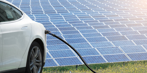 Close up of electric car with a connected charging cable on the background of solar panels	