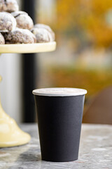 Morning coffee in black paper cup, take-away mug under light and shadown through tree.