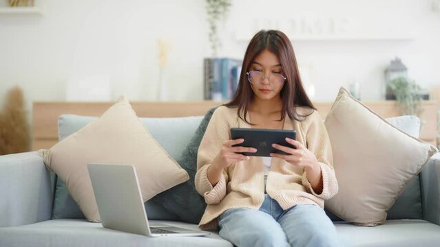 Young asian woman using computer laptop, tablet and mobile smartphone while seated on couch at home