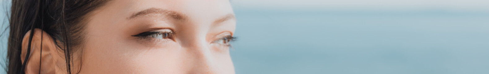 Women's eyes banner. Close up portrait of young caucasian woman with freckles at sunset time and sea background. Cute woman portrait.
