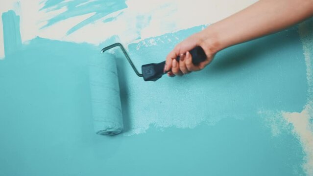 Unrecognizable person applying blue paint on wall. Female hand with roller painting wall. Concept of repair work and improvement of housing conditions.