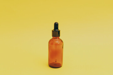 Facial serum in a glass brown bottle on a yellow background, cosmetics commercial shoot