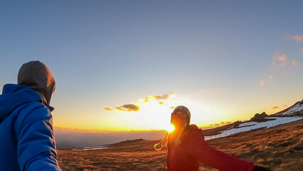 Couple standing on alpine meadow, taking selfies and enjoying beautiful sunset at golden hour on...