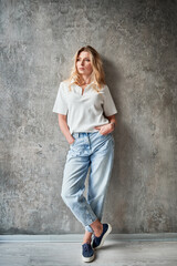 Fototapeta premium Full length of woman in casual clothes standing by the wall in new apartment. Female person keeping hands in jeans pockets..