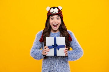 Amazed excited teenage girl child holding gift box on yellow isolated background. Gift for kids birthday. Christmas or New Year present box.