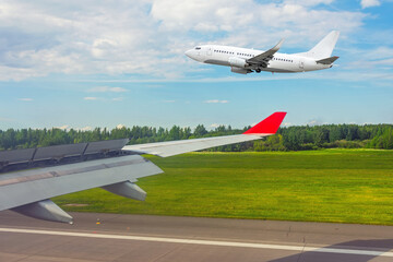 View from the window of the aircraft after landing on the runway and a plane taking off parallel to the side.