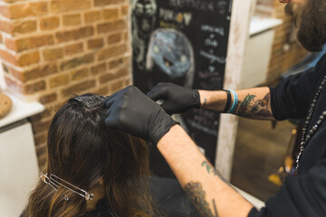 Professional hairdresser in the black hat with beard wearing black gloves dyeing his client's long hair in the professional hair salon. High quality photo