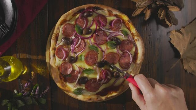 Peda&ccedil;o de pizza sendo cortado em macro. Calabresa, queijo, azeitona e cebolas. C&acirc;mera de cima.