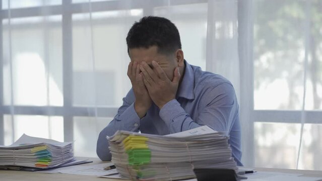 Male office worker in piles of paper folders searching for information on desk of him is clearing a lot of paperwork feeling stressed and hectic at the office.