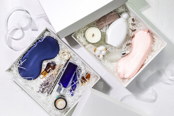 Holiday gift boxes. White gift boxes with sleep care set for men and women. Preparing self care package, craft gift box with mask for sleep, aroma candle, aroma sticks, oil and bubble bath. Flat lay