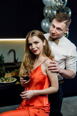 a married couple poses and hugs at a festive table on the occasion of a birthday;
alcohol and snacks are on the table;
glasses with red wine in hands;
boy and girl express sincere feelings