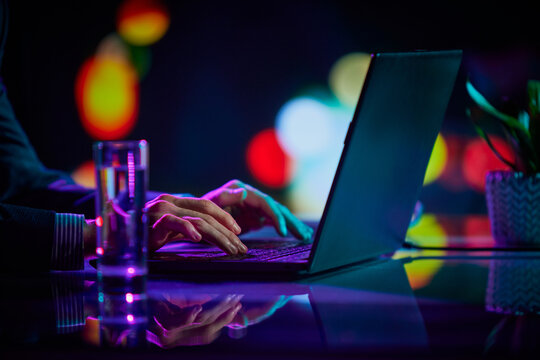 Cropped Image Of Male Hands Of IT Specialist Typing On Laptop Keyboard At Evening Time. Cool Colored Neon Hue Lights In Office Space.