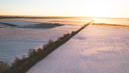 Aerial view of the snowy fields during sundown. Solar panels in the distance.
