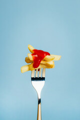 close-up of french fries with ketchup sauce chopped on a fork on a blue background