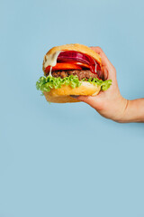 close-up on a hamburger in a female hand on a blue background