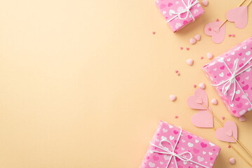 Valentine's Day concept. Top view photo of pink present boxes paper hearts on sticks and sprinkles on isolated pastel beige background with empty space