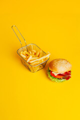 close-up of french fries in a basket and a hamburger on yellow background with free space for text