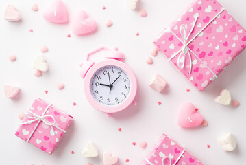 Valentine's Day concept. Top view photo of pink alarm clock gift boxes heart shaped marshmallow candles and sprinkles on isolated white background